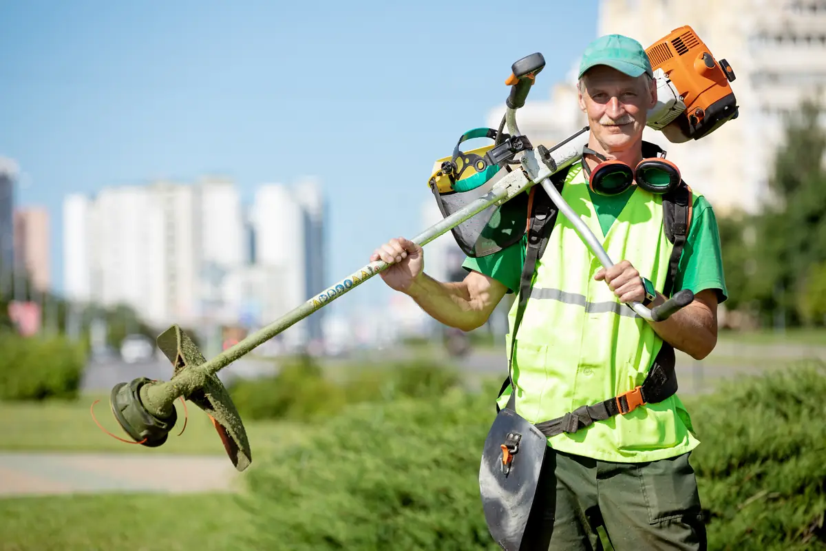 Landscaping crew member carrying a string trimmer on a job site